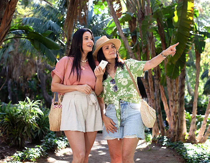 Duas mulheres num cenário de férias, a olhar na direção para onde uma delas aponta. Uma das mulheres tem na mão um Vasco Translator V4.