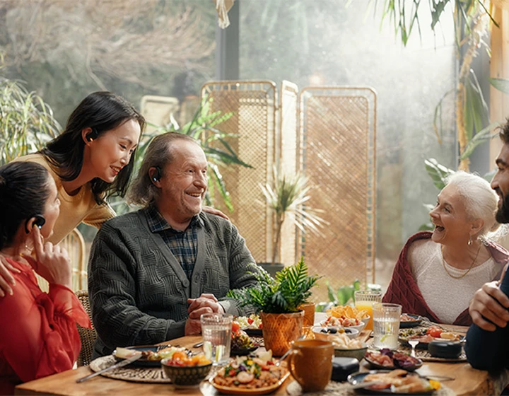 Uma família sentada à volta de uma mesa, com os auscultadores Vasco Translator E1, a rir e a conversar entre si.