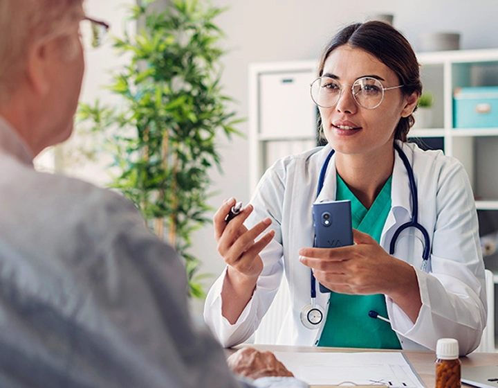 Médica a segurar o tradutor Vasco V4 e a falar com um paciente durante uma consulta.