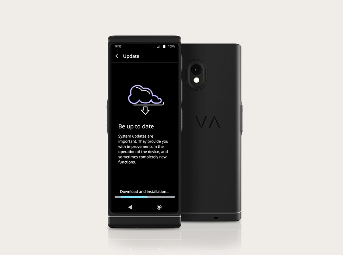 Uma fotografia de produto em estúdio do 
Vasco Translator
 V4, mostrando a interface de atualização do sistema. Dois dispositivos pretos estão posicionados lado a lado: um virado para a frente e outro mostrando a parte traseira. O ecrã exibe um ícone de nuvem com uma seta de download, o título «Mantenha-se atualizado» e uma barra de progresso na parte inferior com a indicação «Download e instalação...». A vista traseira mostra a câmara de lente dupla e o logótipo «VA» em relevo.